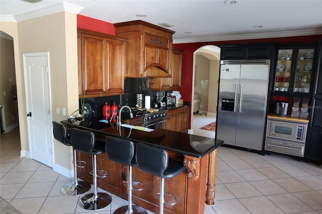 kitchen featuring fridge, stove, light tile floors, backsplash, and a kitchen breakfast bar