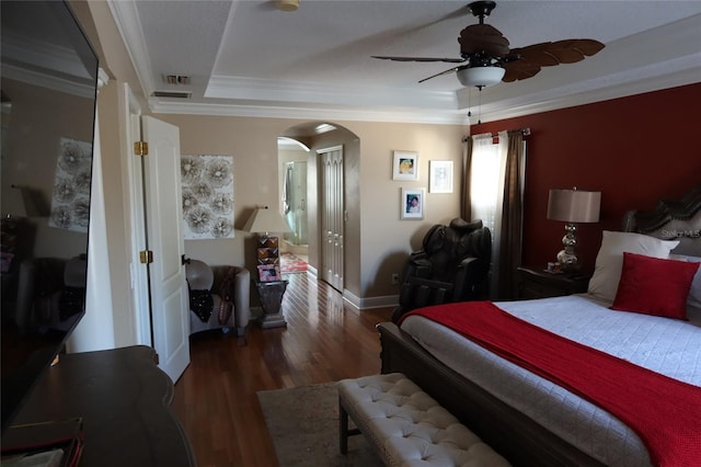 bedroom with crown molding, dark hardwood / wood-style flooring, ceiling fan, and a tray ceiling