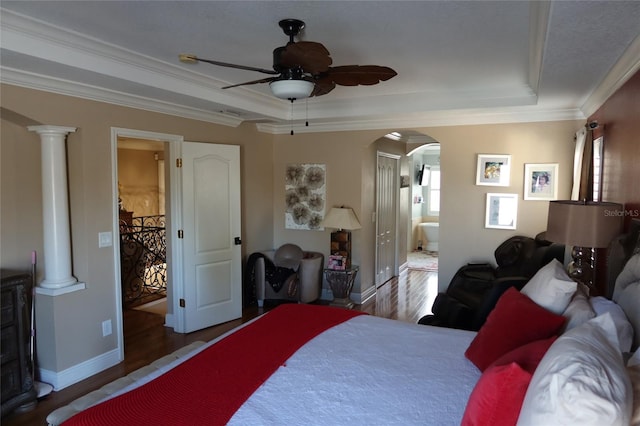 bedroom with ceiling fan, dark hardwood / wood-style flooring, ensuite bathroom, a tray ceiling, and ornate columns