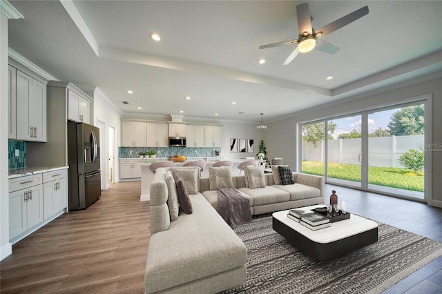 living room with hardwood / wood-style floors, ceiling fan, a raised ceiling, and ornamental molding