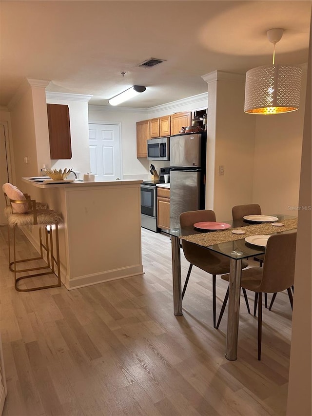 kitchen with crown molding, a breakfast bar area, light wood-type flooring, kitchen peninsula, and stainless steel appliances