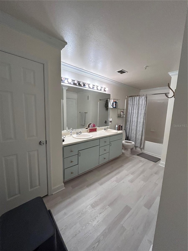 full bathroom with wood-type flooring, a textured ceiling, toilet, vanity, and ornamental molding