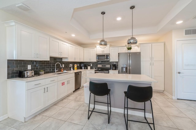 kitchen with a raised ceiling, a kitchen island, white cabinets, stainless steel appliances, and decorative light fixtures