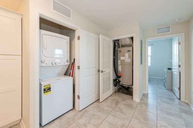 clothes washing area featuring stacked washer and clothes dryer, light tile floors, and heating utilities