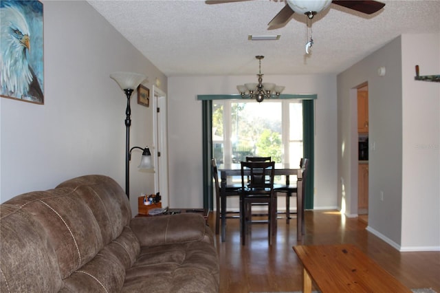 living room featuring a textured ceiling, ceiling fan with notable chandelier, and dark wood-type flooring