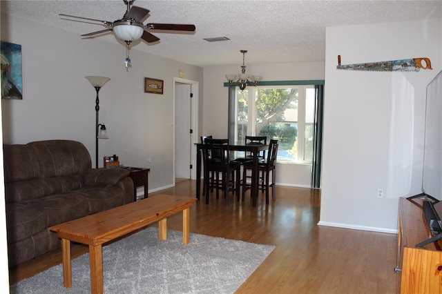 living room with wood-type flooring, ceiling fan with notable chandelier, and a textured ceiling