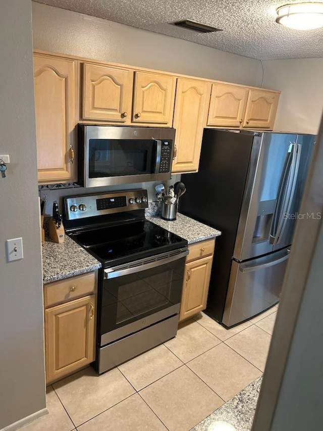 kitchen featuring light brown cabinets, light stone counters, a textured ceiling, light tile patterned flooring, and appliances with stainless steel finishes