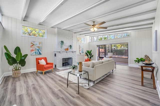 living room featuring a fireplace, brick wall, ceiling fan, beamed ceiling, and light hardwood / wood-style flooring