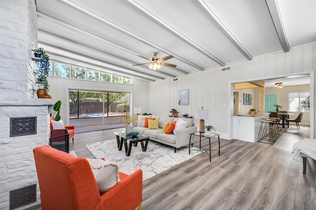 living room with light hardwood / wood-style floors, ceiling fan, a tile fireplace, and beamed ceiling