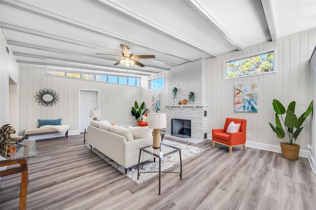 living room with beamed ceiling, a stone fireplace, ceiling fan, and light wood-type flooring