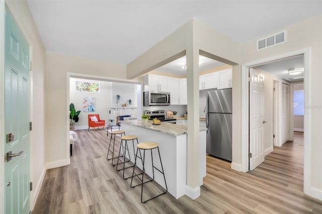 kitchen with appliances with stainless steel finishes, white cabinetry, a breakfast bar, and light hardwood / wood-style flooring