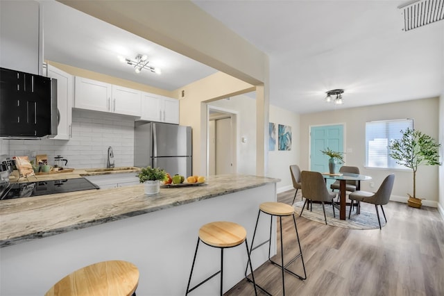 kitchen featuring white cabinets, stainless steel refrigerator, light stone countertops, a kitchen bar, and light wood-type flooring