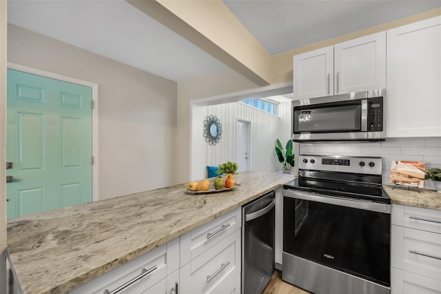 kitchen with tasteful backsplash, white cabinets, appliances with stainless steel finishes, and light stone countertops