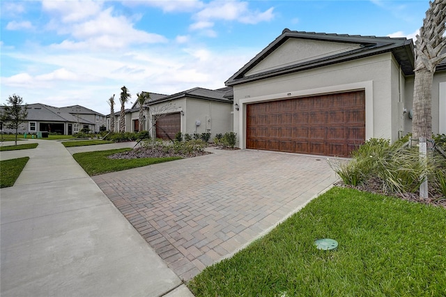 ranch-style house with a front yard, decorative driveway, an attached garage, and stucco siding