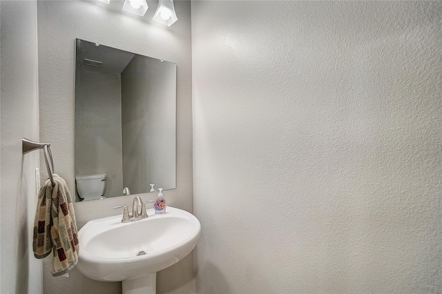 bathroom featuring a textured wall, a sink, and toilet