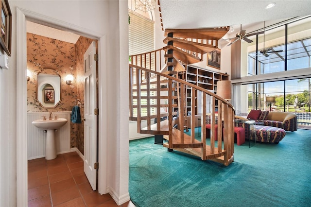 stairs featuring a high ceiling, dark tile flooring, ceiling fan, and a textured ceiling