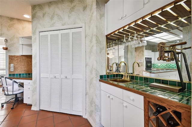 bar featuring dark tile floors, tile counters, white cabinets, sink, and black oven