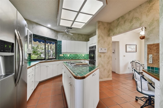 kitchen with appliances with stainless steel finishes, tile counters, ceiling fan, white cabinets, and light tile floors