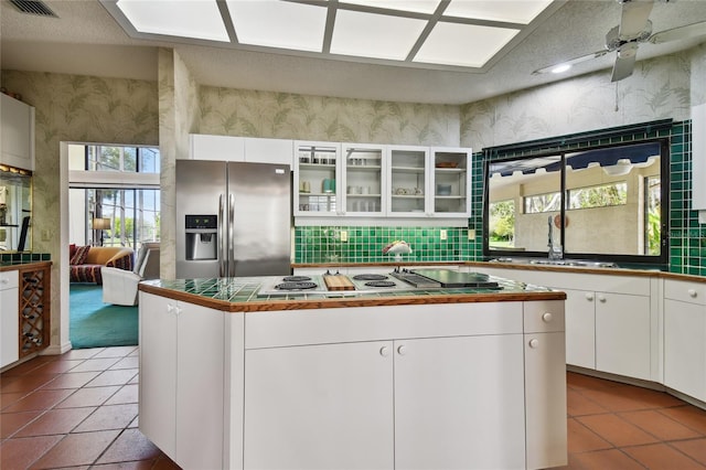 kitchen featuring a kitchen island, ceiling fan, stainless steel appliances, tile flooring, and white cabinetry