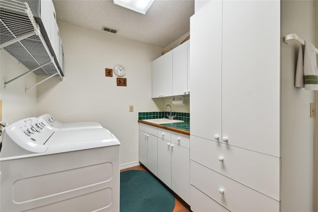 laundry area featuring a textured ceiling, washing machine and clothes dryer, cabinets, and sink