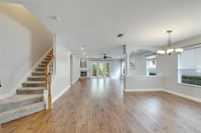 unfurnished living room with a wealth of natural light, ceiling fan with notable chandelier, and light wood-type flooring