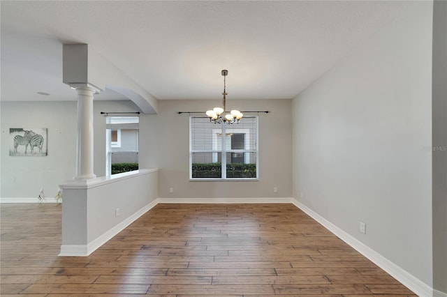 spare room with hardwood / wood-style flooring, decorative columns, and a notable chandelier