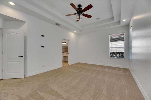 unfurnished room with ceiling fan, a raised ceiling, and light colored carpet