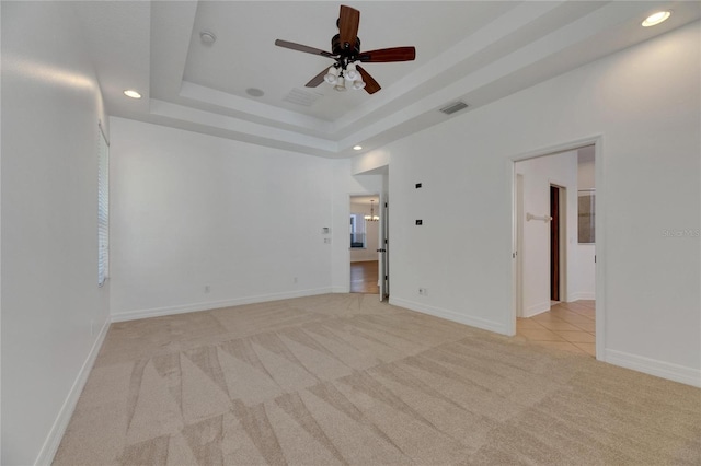 unfurnished room featuring ceiling fan, a raised ceiling, and light carpet