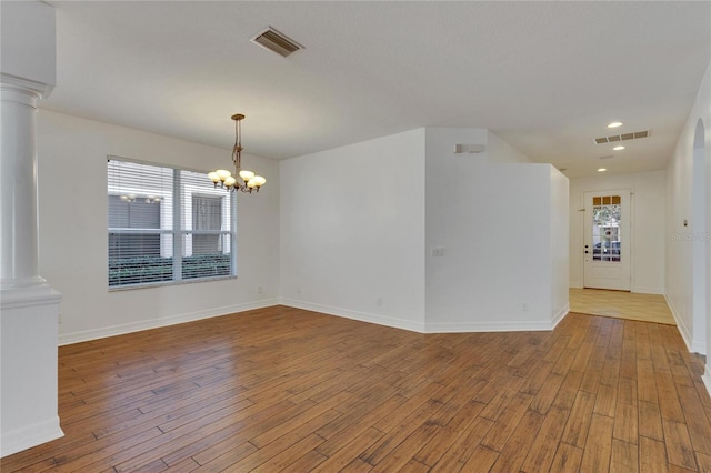 empty room with a notable chandelier, plenty of natural light, and light wood-type flooring