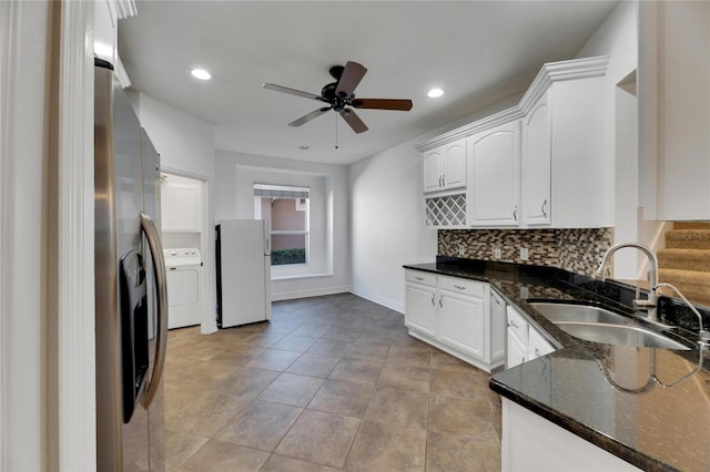 kitchen with dark stone counters, white refrigerator, sink, washer / dryer, and white cabinetry