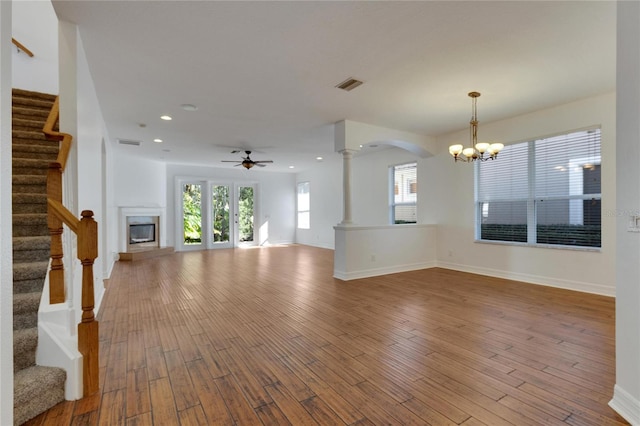 unfurnished living room with ceiling fan with notable chandelier, wood-type flooring, and ornate columns