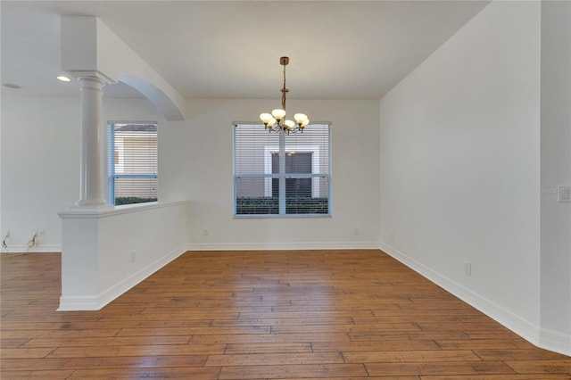 unfurnished dining area featuring hardwood / wood-style floors, ornate columns, and a chandelier