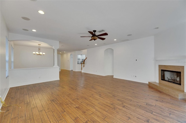 unfurnished living room with ceiling fan with notable chandelier and light hardwood / wood-style floors