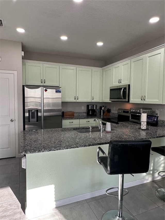 kitchen featuring a kitchen bar, sink, dark stone countertops, stainless steel appliances, and white cabinets