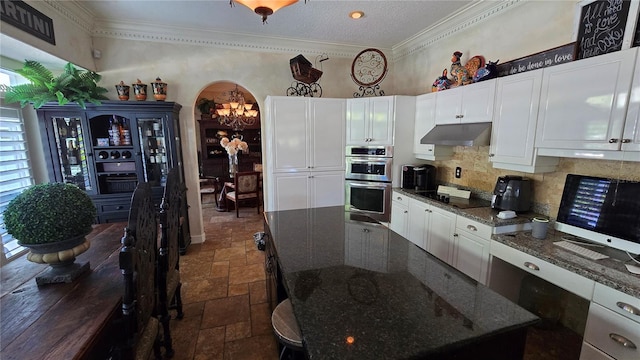 kitchen with white cabinetry, stainless steel double oven, backsplash, dark stone counters, and a center island