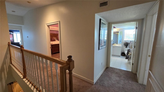 corridor with a textured ceiling, dark carpet, and a wealth of natural light