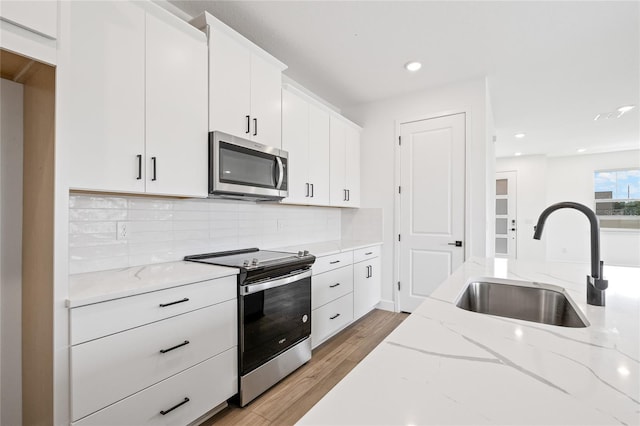 kitchen with appliances with stainless steel finishes, sink, light stone countertops, white cabinetry, and light hardwood / wood-style floors