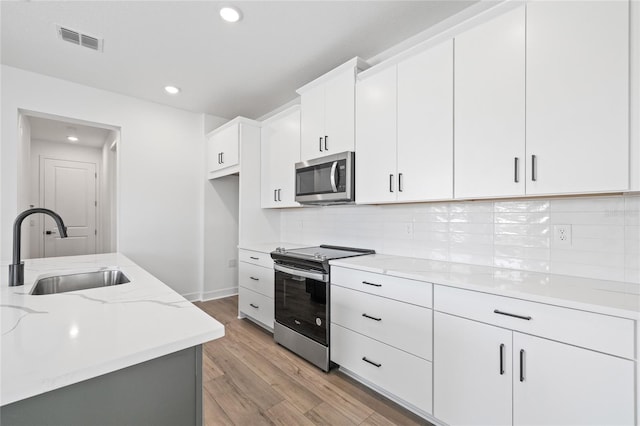 kitchen with white cabinets, light stone counters, appliances with stainless steel finishes, light wood-type flooring, and sink