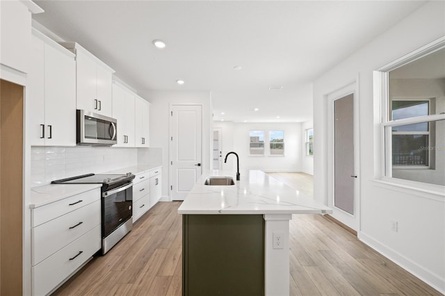 kitchen featuring a kitchen island with sink, sink, light wood-type flooring, white cabinetry, and appliances with stainless steel finishes