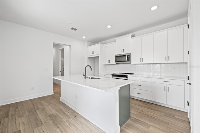 kitchen with white cabinetry, stainless steel appliances, sink, and an island with sink