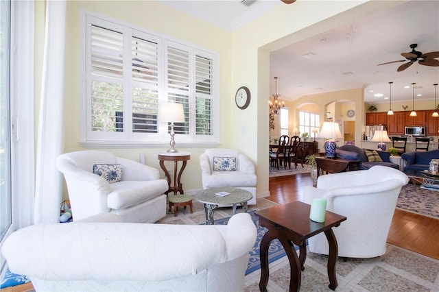 living room with crown molding, ceiling fan with notable chandelier, and light wood-type flooring