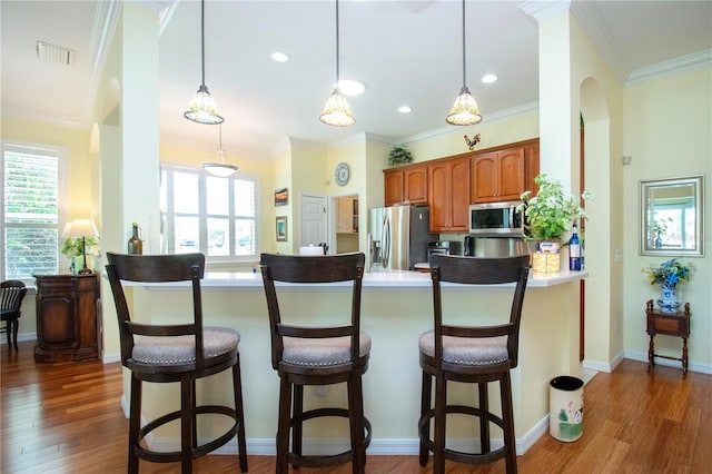 kitchen with pendant lighting, a kitchen breakfast bar, kitchen peninsula, appliances with stainless steel finishes, and dark hardwood / wood-style floors