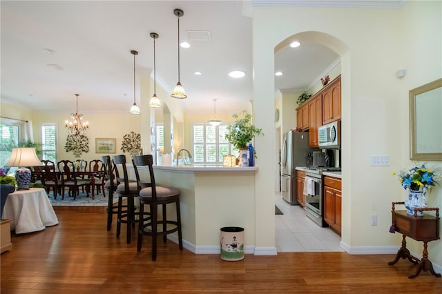 kitchen with hanging light fixtures, appliances with stainless steel finishes, a breakfast bar area, a notable chandelier, and light wood-type flooring