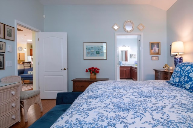 bedroom with connected bathroom, vaulted ceiling, and hardwood / wood-style flooring