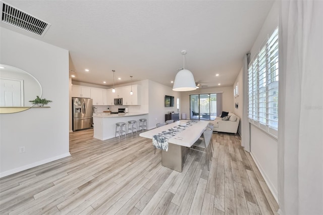 interior space featuring appliances with stainless steel finishes, a breakfast bar area, white cabinetry, light wood-type flooring, and hanging light fixtures