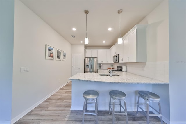 kitchen with stainless steel appliances, tasteful backsplash, light hardwood / wood-style flooring, white cabinetry, and hanging light fixtures