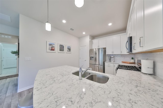 kitchen with hardwood / wood-style floors, tasteful backsplash, stainless steel appliances, decorative light fixtures, and white cabinets