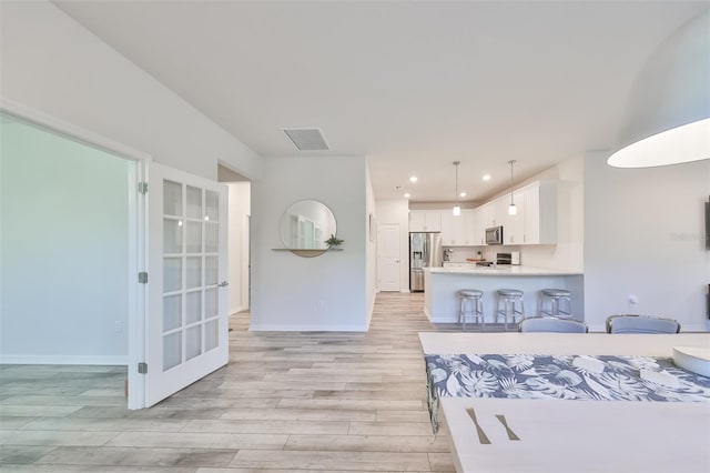 kitchen featuring pendant lighting, a kitchen breakfast bar, light hardwood / wood-style floors, appliances with stainless steel finishes, and white cabinetry