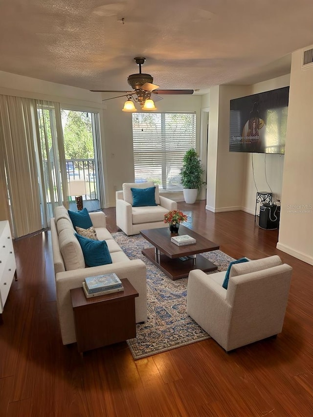 living room with wood finished floors, plenty of natural light, a ceiling fan, baseboards, and a textured ceiling