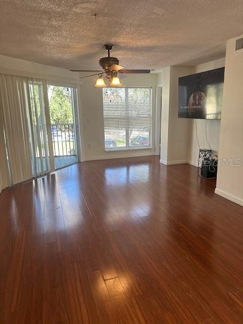 unfurnished living room featuring a textured ceiling, ceiling fan, wood finished floors, and baseboards